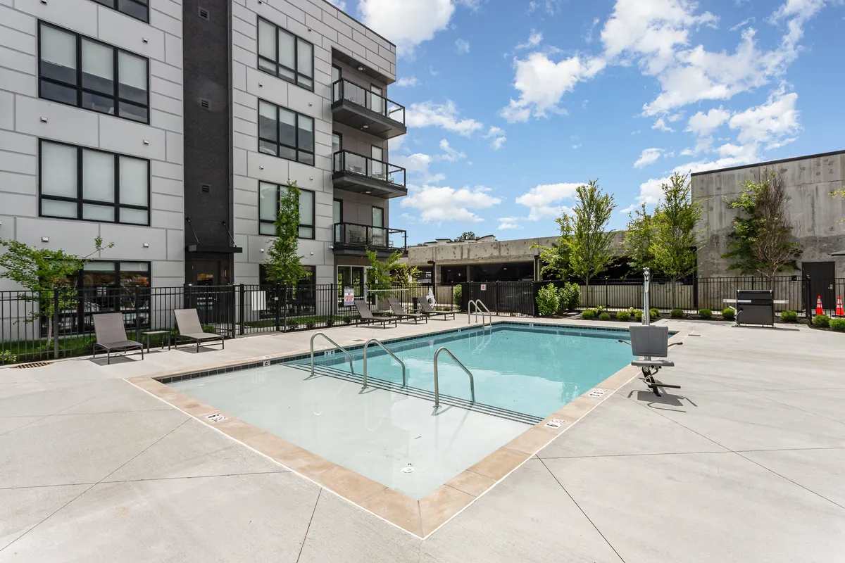 This image showcases a sparkling swimming pool with lounge chairs and a beautifully landscaped area, set against the backdrop of a modern building with balconies. The space is inviting for both relaxation and social gatherings, with ample seating and greenery that create a resort-style atmosphere.