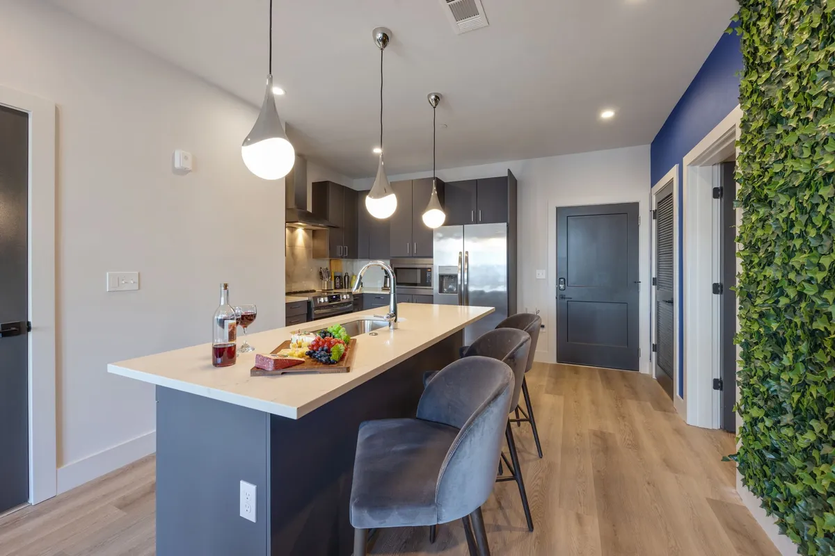 A stylish kitchen island with bar stools, a bottle of wine, a fruit and cheese platter, and a green accent wall. This scene exudes a sense of casual dining and socializing, suggesting ease of entertaining and a welcoming atmosphere for both meal prep and gathering.
