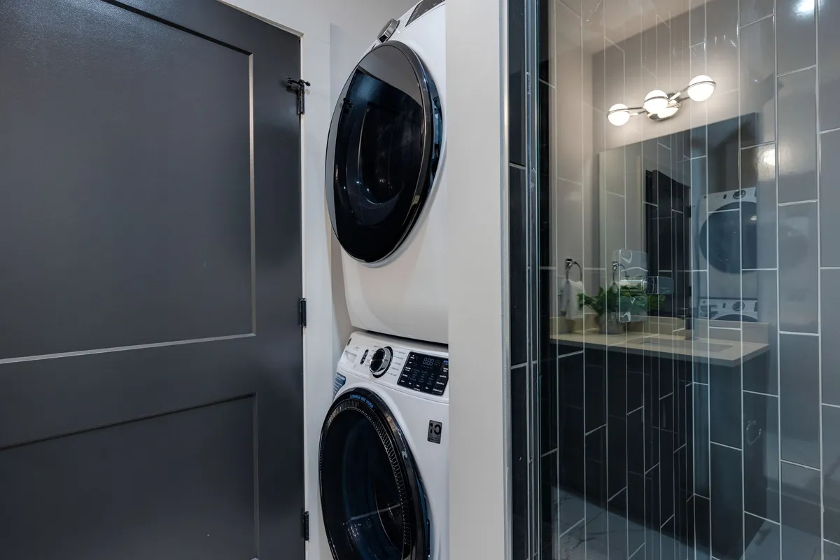 A clean utility area featuring a stacked washer and dryer, mirror, vanity, and organized storage. The space is efficient, bright, and practical for longer stays.